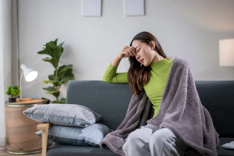 Woman sitting on a sofa with chills and feeling unwell