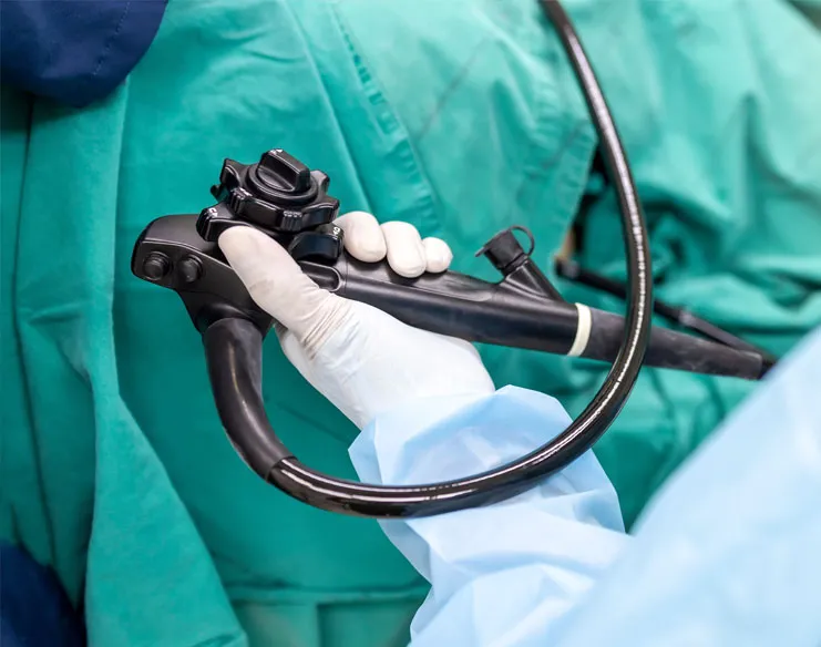 Doctor wearing a light blue protective surgical gown and gloves preparing for a colonoscopy procedure.
