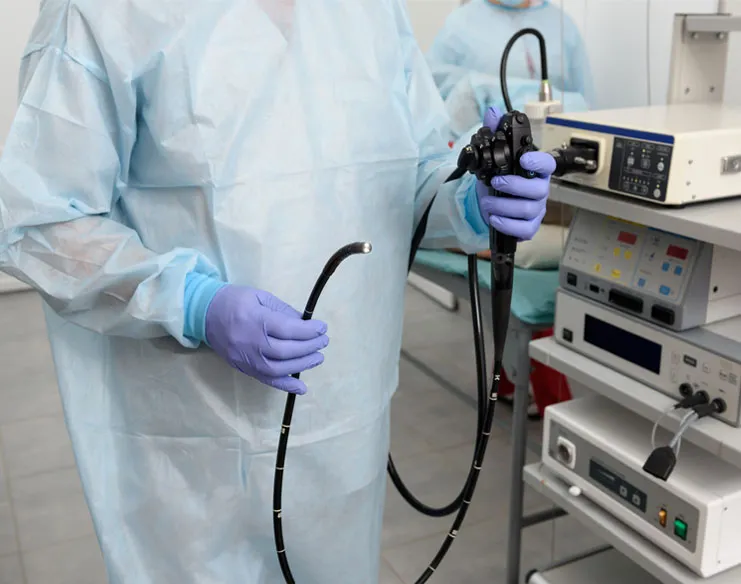 Instruments for colonoscopy being held by a doctor wearing blue gloves.