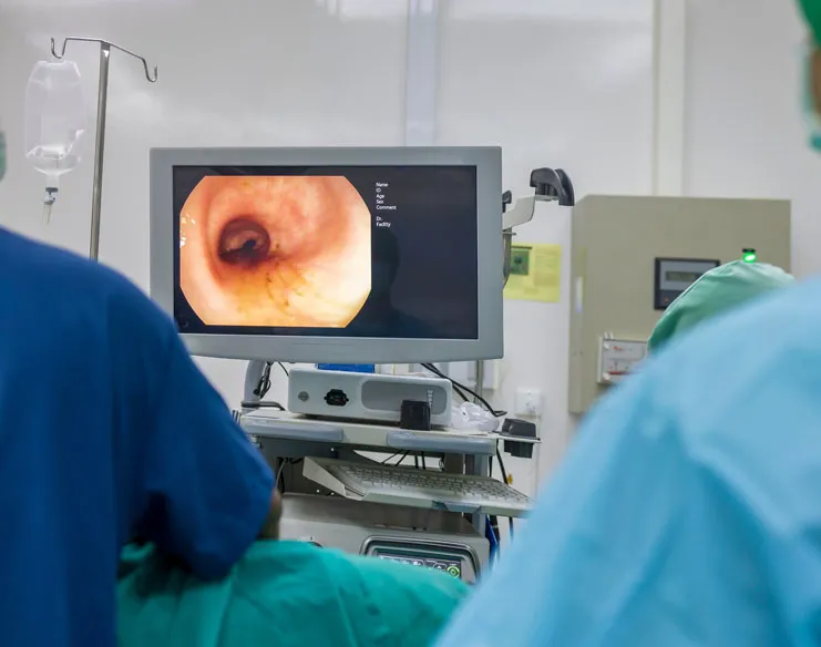 Surgeon in a light blue protective gown and cap preparing for a colonoscopy procedure.