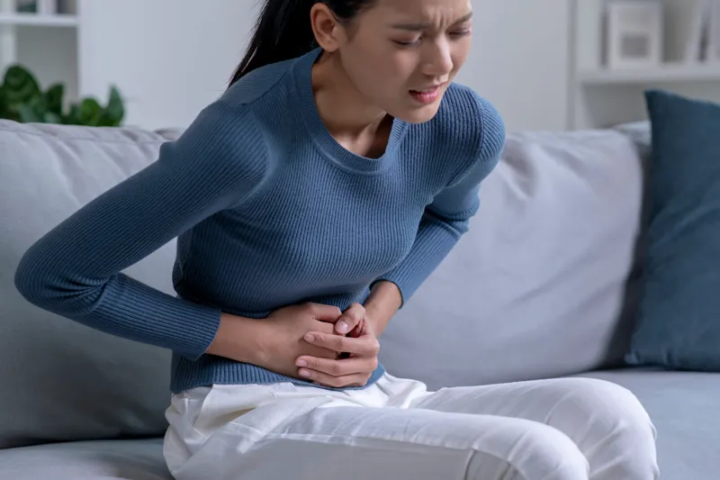 Woman sitting on a sofa holding her lower abdomen with a pained expression