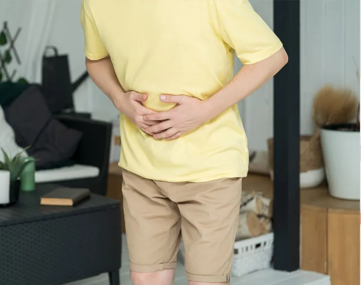 Man experiencing abdominal discomfort while holding his stomach at home.