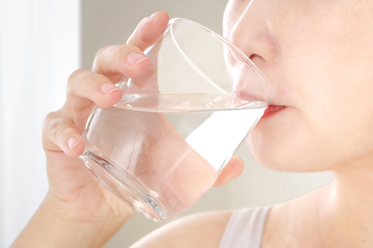 Woman drinking a glass of water to stay hydrated as part of lifestyle care.