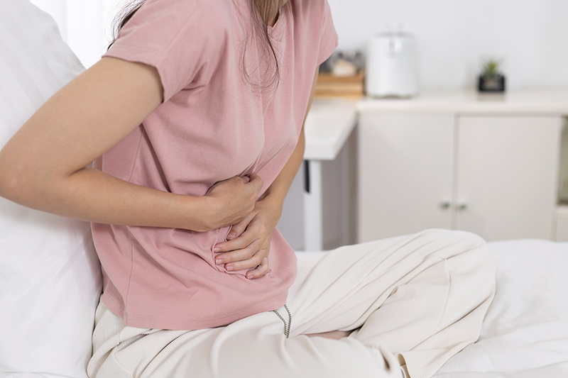 Woman sitting and holding her abdomen in discomfort, indicating abdominal pain.