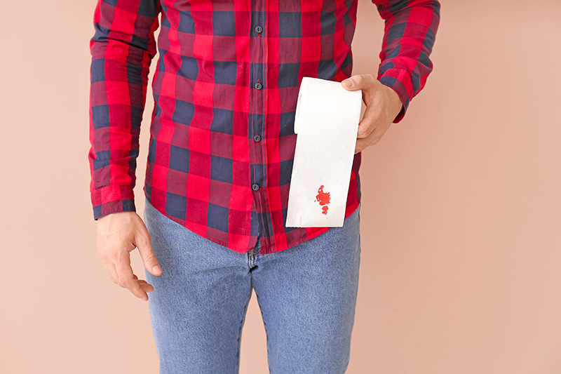 Man holding toilet paper with visible blood suggesting rectal bleeding.