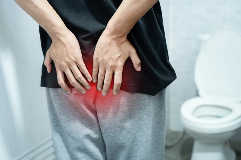 Man experiencing discomfort from piles while standing in front of a toilet